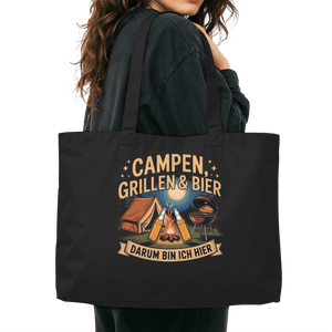 Woman carrying black organic shopping bag with 'Campen, Grillen & Bier' design, perfect for eco-friendly weekend trips.