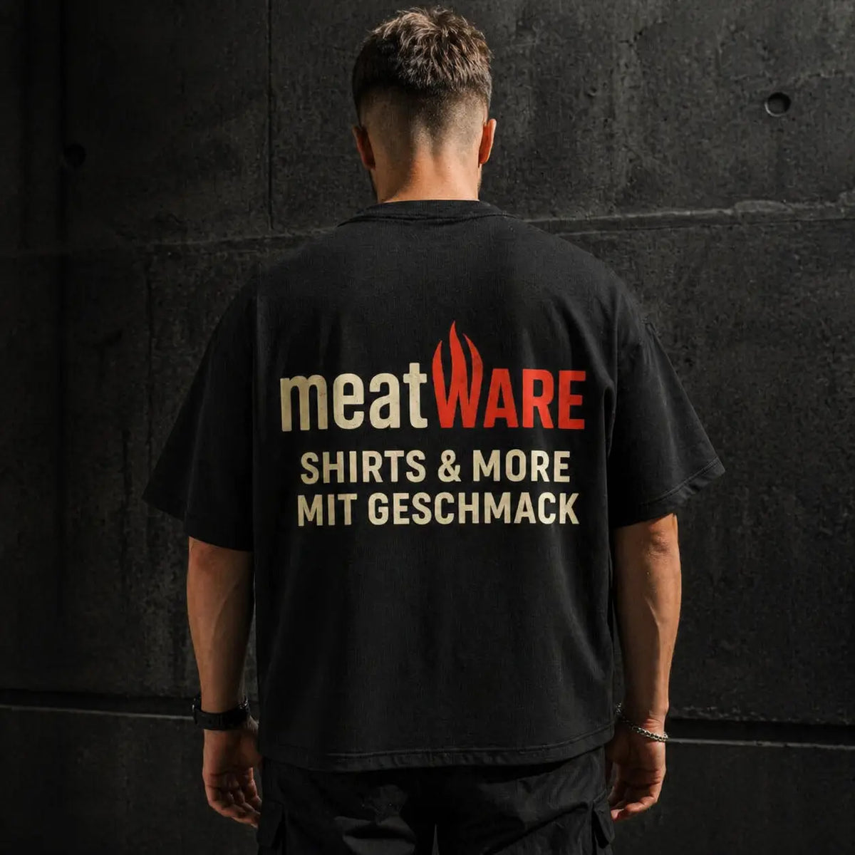 Oversized schwarzes Meatware T-Shirt mit großem Backprint „Shirts & More mit Geschmack“, getragen vor dunkler Betonwand, Streetwear Look mit lockerem Schnitt und starkem Markenstatement im Fokus