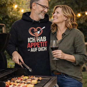 Paar beim Grillen trägt schwarzen Meatware Premium Hoodie mit Spaghetti-Herz-Motiv und Schriftzug „Ich hab Appetit auf Dich“ – Liebesdesign zum Thema Liebe geht durch den Magen