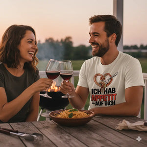 Paar lacht und stößt mit Rotwein an; Mann trägt T-Shirt „Ich hab Appetit auf Dich“, Spaghetti-Herz, Meatware-Stil, Grillabend