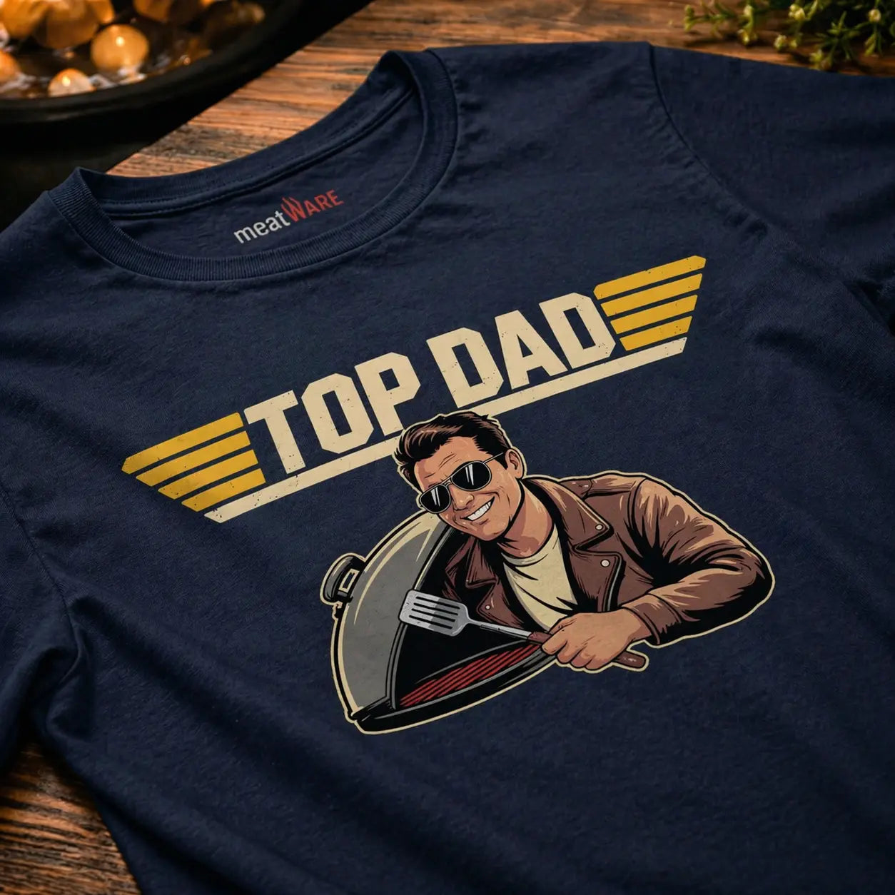 Nahaufnahme eines navyfarbenen Premium T-Shirts mit „Top Dad“ Grillmotiv und Nackenbranding im rustikalen BBQ Mockup auf Holzoberfläche als Vatertags Geschenkidee