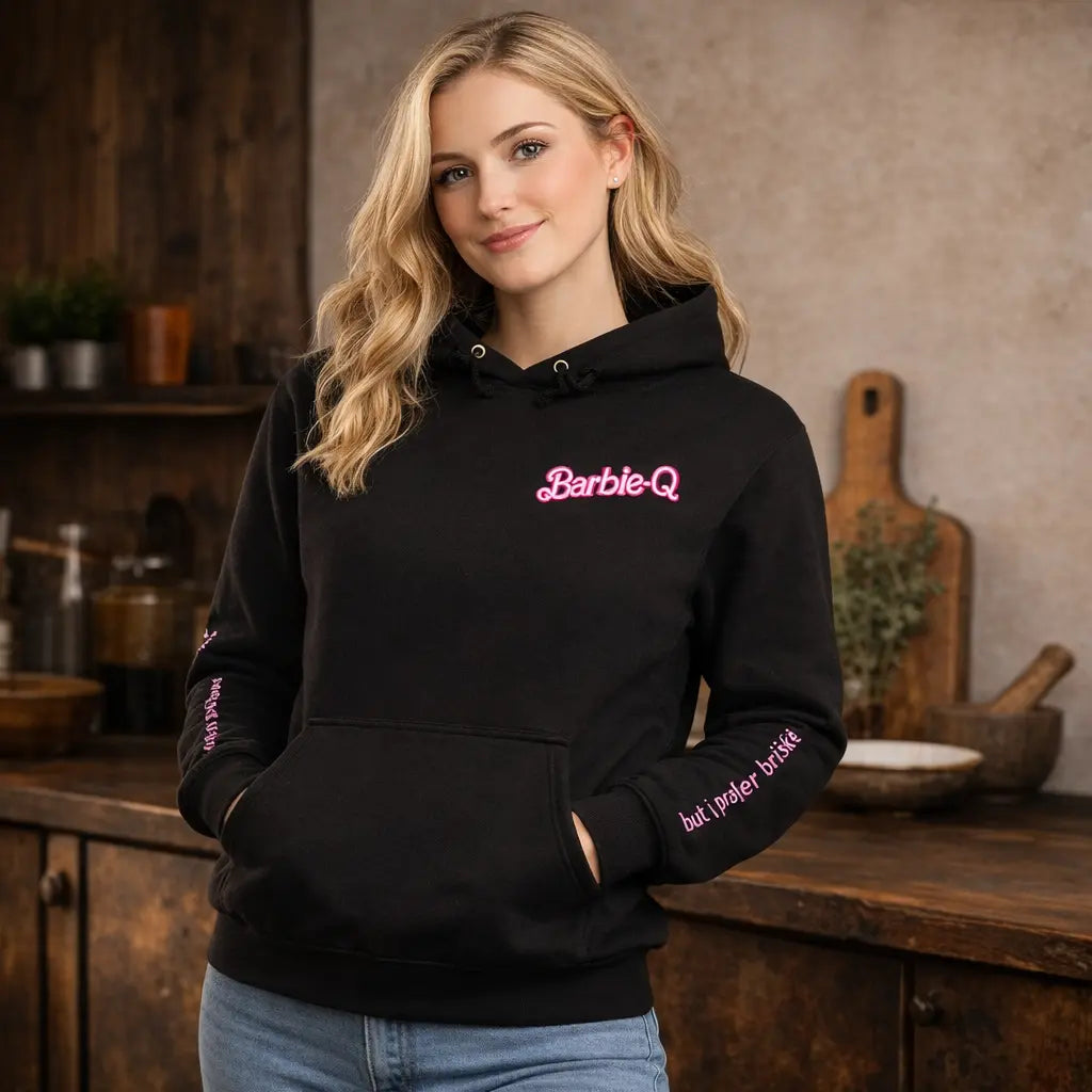 Woman wearing black Barbie-Q BBQ hoodie with pink logo and sleeve text, Meatware grill hoodie shown in rustic kitchen lifestyle mockup