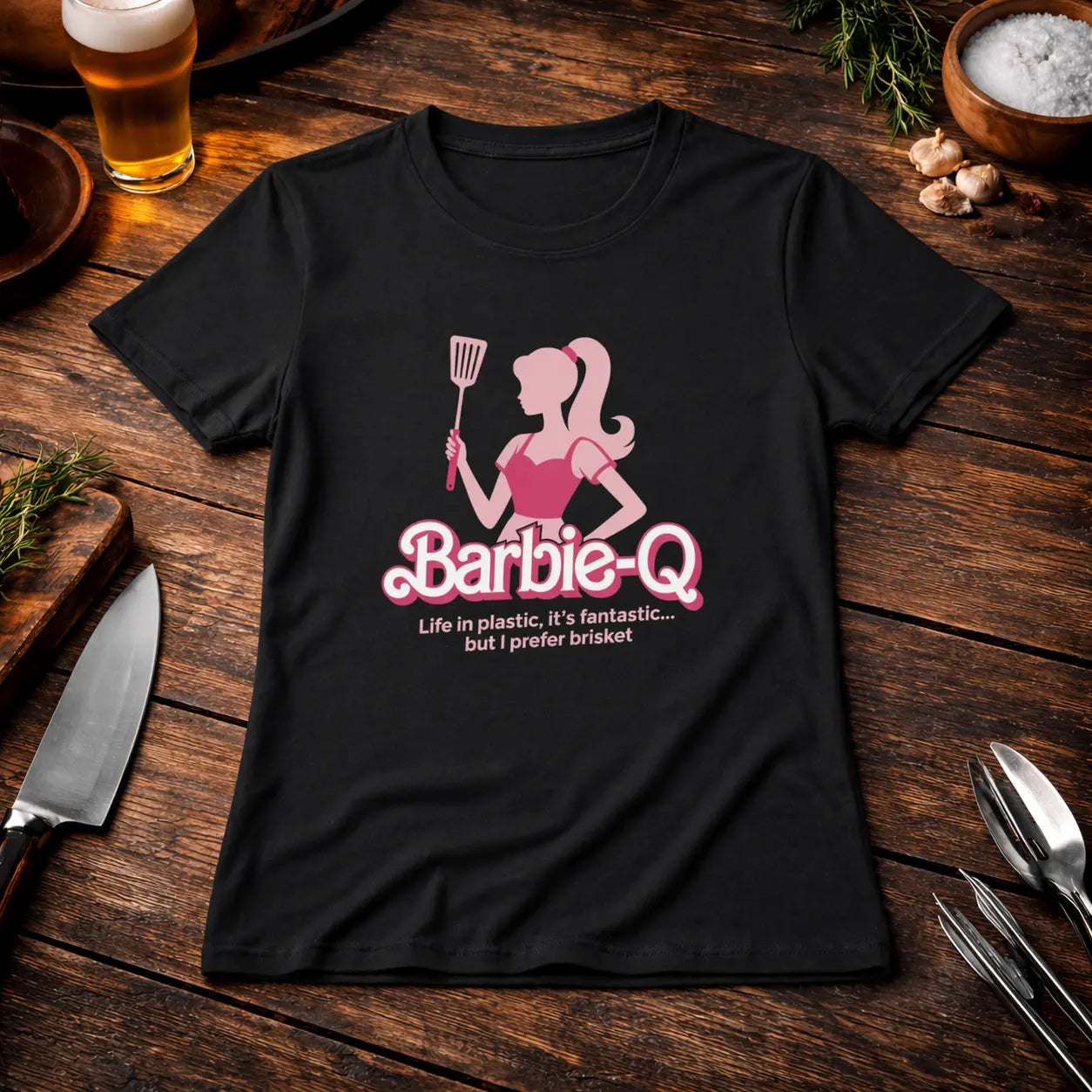 Premium Organic Women T-Shirt with Barbie-Q brisket BBQ design on black shirt, styled on rustic wooden table with beer, grill tools and herbs – Meatware Shirts & more mit Geschmack