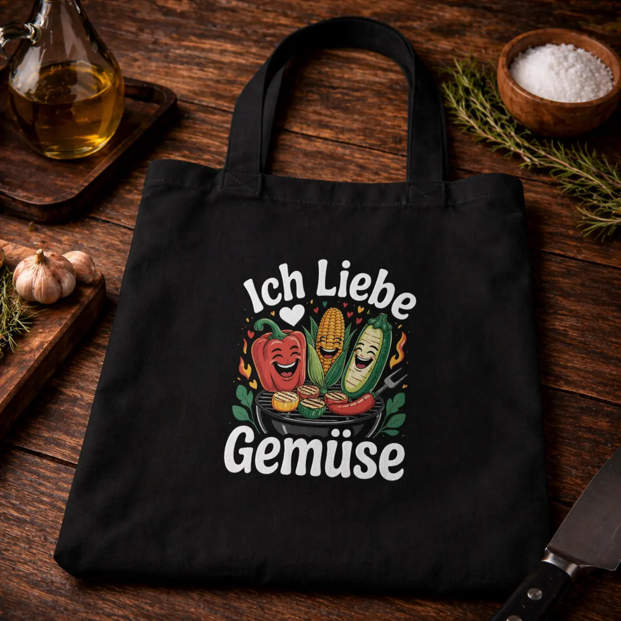 Black tote bag with Ich liebe Gemüse BBQ vegetable design, placed on rustic wooden table with garlic, herbs, oil and kitchen tools – Meatware Shirts & more mit Geschmack