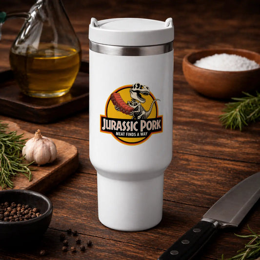 White insulated travel mug with Jurassic Pork BBQ dinosaur design, placed on rustic wooden table with garlic, herbs, oil and kitchen tools – Meatware Shirts & more mit Geschmack