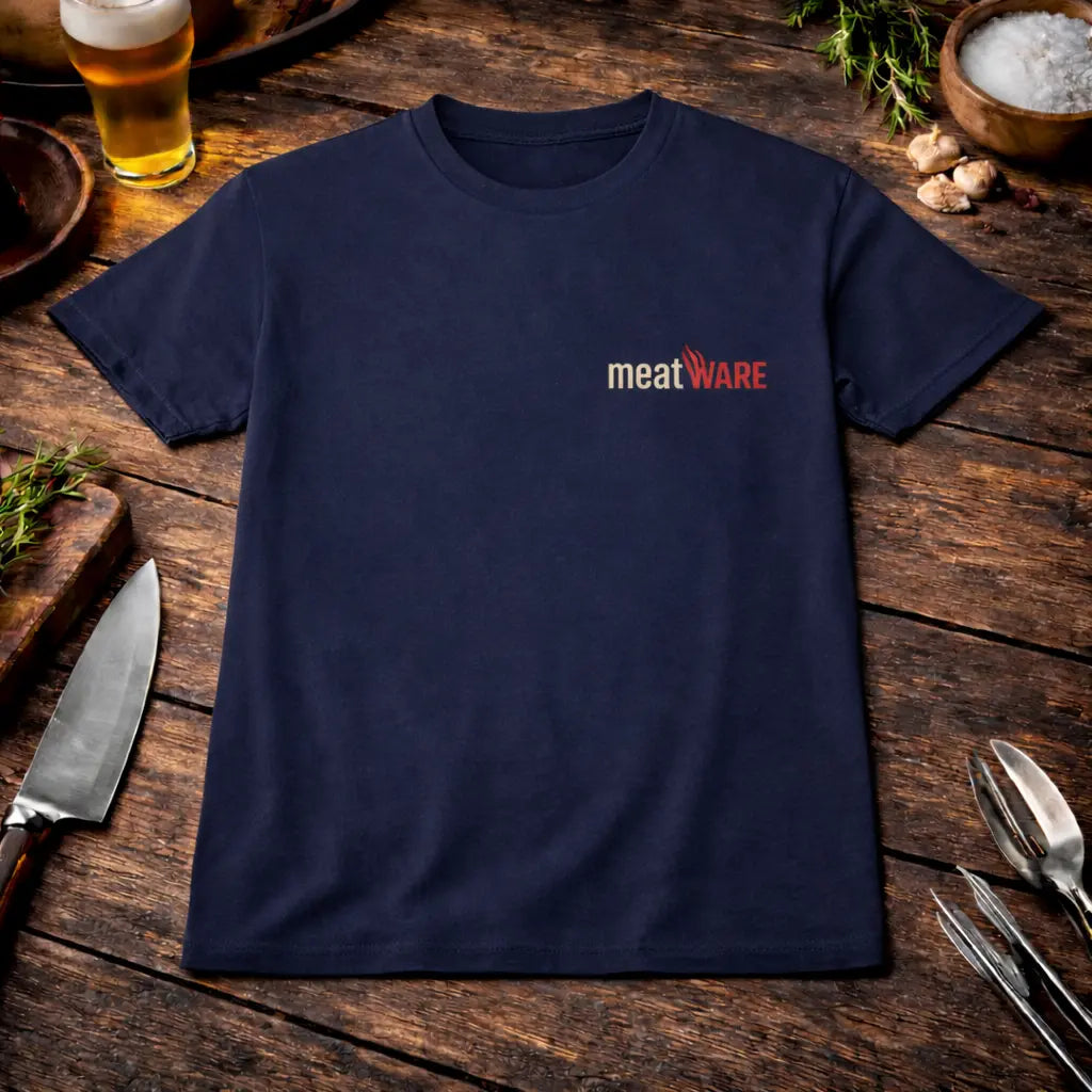 Navy blaues T-Shirt mit kleinem Meatware Logo auf der Brust und zusätzlichem Meatware Nackenbranding im rustikalen BBQ Mockup auf Holztisch mit Bier, Knoblauch und Grillbesteck