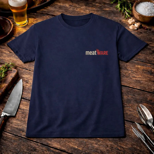 Navy blaues T-Shirt mit kleinem Meatware Logo auf der Brust und zusätzlichem Meatware Nackenbranding im rustikalen BBQ Mockup auf Holztisch mit Bier, Knoblauch und Grillbesteck