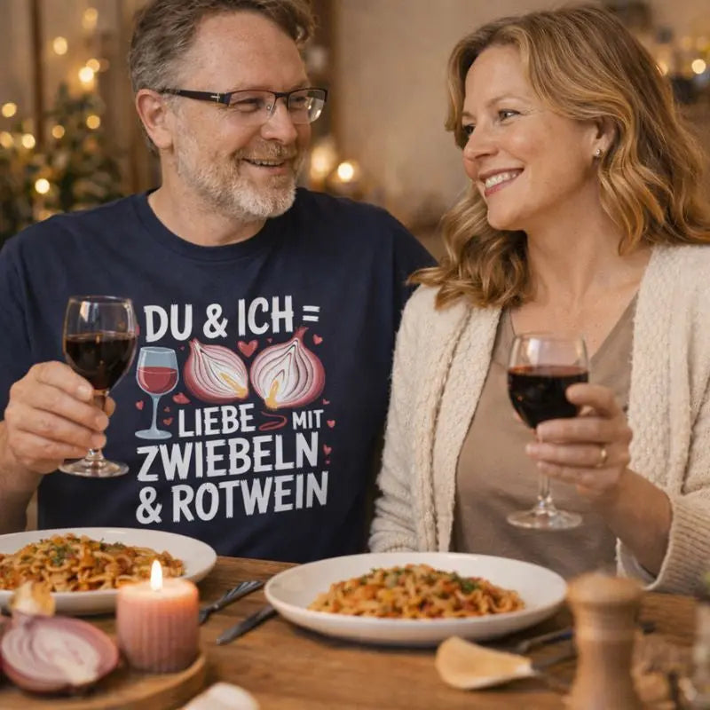 Paar sitzt beim romantischen Dinner und trägt Meatware Premium T-Shirt mit Spruch ›Du & Ich – Liebe mit Zwiebeln & Rotwein‹ – humorvolles Liebesmotiv zum Thema Liebe geht durch den Magen