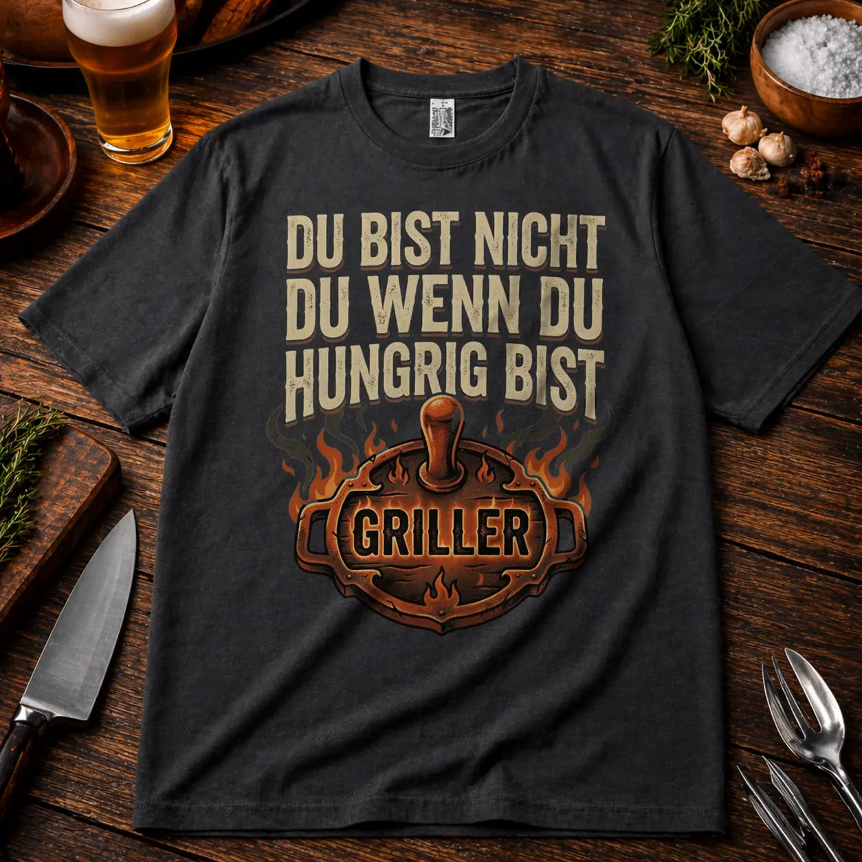 Oversized T-Shirt in Dunkelgrau mit „Du bist nicht du wenn du hungrig bist Griller“ BBQ Motiv auf rustikalem Holztisch Mockup mit Bier und Grillzubehör