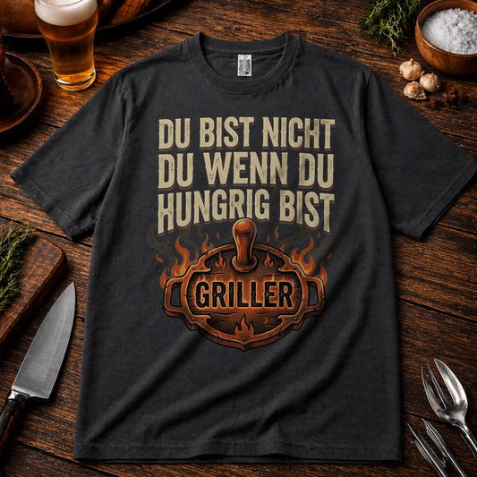 Oversized T-Shirt in Dunkelgrau mit „Du bist nicht du wenn du hungrig bist Griller“ BBQ Motiv auf rustikalem Holztisch Mockup mit Bier und Grillzubehör