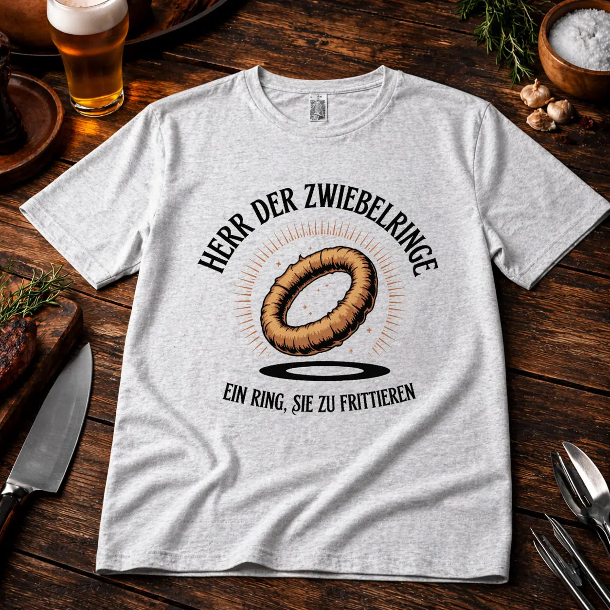 Graues Premium T-Shirt mit lustigem BBQ Design „Herr der Zwiebelringe – Ein Ring sie zu frittieren“ im rustikalen Grill Mockup auf Holztisch mit Bier, Gewürzen und Grillbesteck