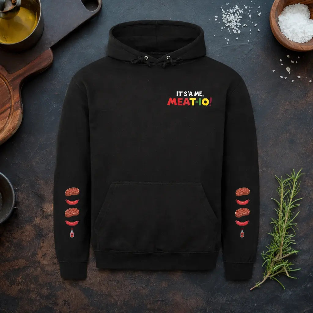 Meatware BBQ Gamer Hoodie mit Schriftzug "It's a Me Meat-io" auf schwarzem Hoodie in rustikalem Küchenmockup mit Messer, Rosmarin und Salz