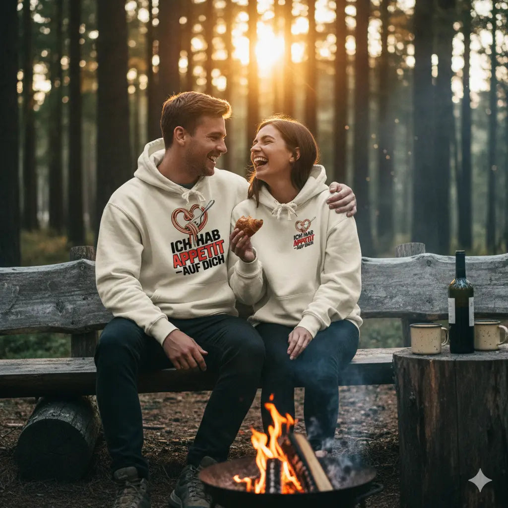 Paar in cremefarbenen Oversized Hoodies mit "Ich hab Appetit auf dich"-Print am Lagerfeuer, Sonnenuntergang im Wald.