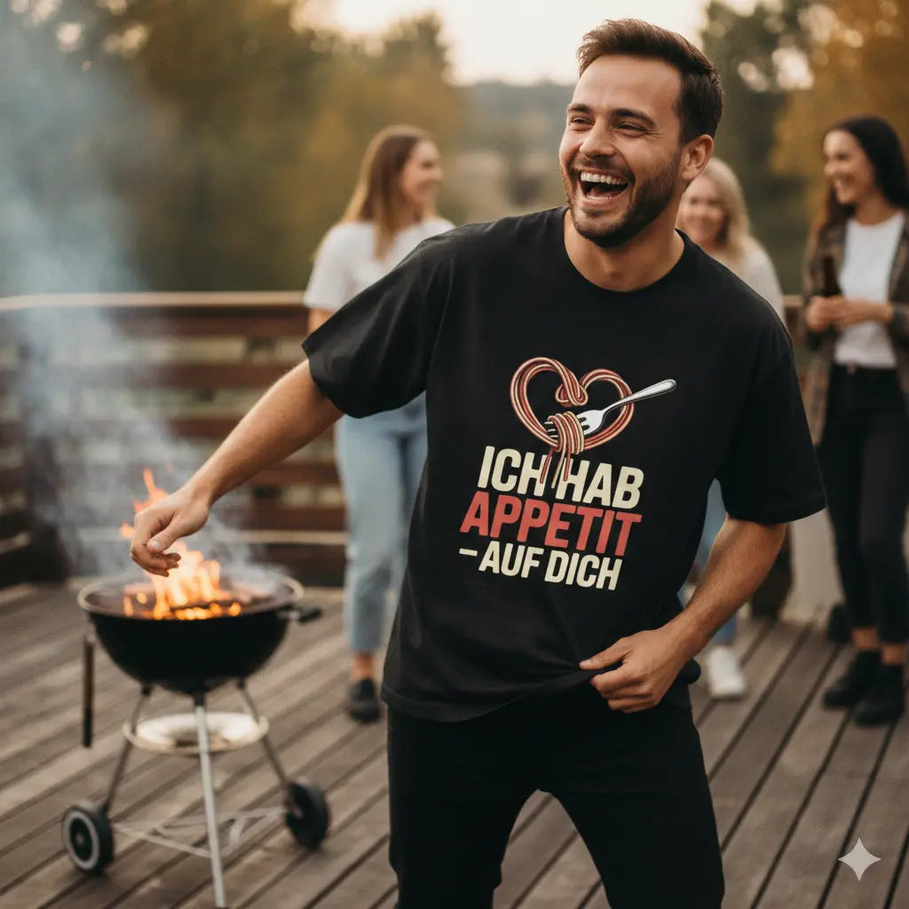Lachender Mann am Grill trägt schwarzes "Ich hab Appetit auf dich" Oversized Shirt, rustikaler Vibe, warmes Abendlicht.
