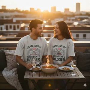 Paar in grauen Oversized T-Shirts mit „Gemeinsam schmeckt’s besser“ Design genießt Essen auf einer Dachterrasse bei Abendlicht