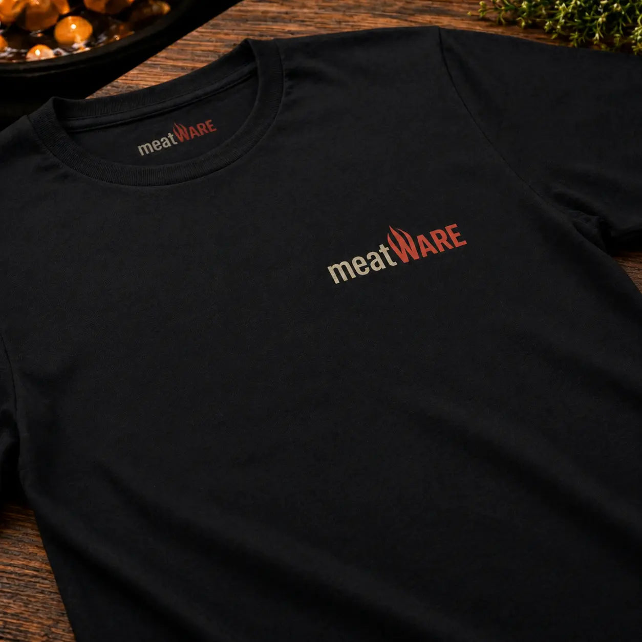 Schwarzes Premium T-Shirt mit kleinem meatWARE Logo auf der Brust in Nahaufnahme auf Holztisch, minimalistisches Basic Shirt mit Nackenbranding und hochwertigem Stoff