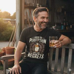 Authentischer Mann lacht mit Whiskey-Glas auf Holzbank, trägt das schwarze Meatware T-Shirt mit dem Motiv 'Aged to Perfection - Just like regrets'