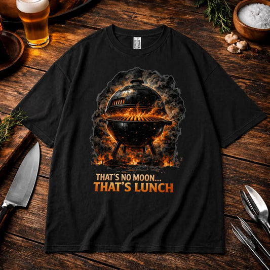 Schwarzes Oversized T-Shirt mit BBQ Grill Motiv „That’s No Moon That’s Lunch“ im rustikalen Grill Mockup mit Bier, Gewürzen und Küchenutensilien auf Holztisch