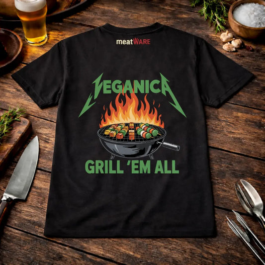 Schwarzes BBQ T-Shirt mit „Veganica Grill ’Em All“ Design mit Gemüsegrill im rustikalen Meatware Mockup auf Holztisch mit Bier, Knoblauch und Grillbesteck sowie Meatware Logo im Nackenbereich