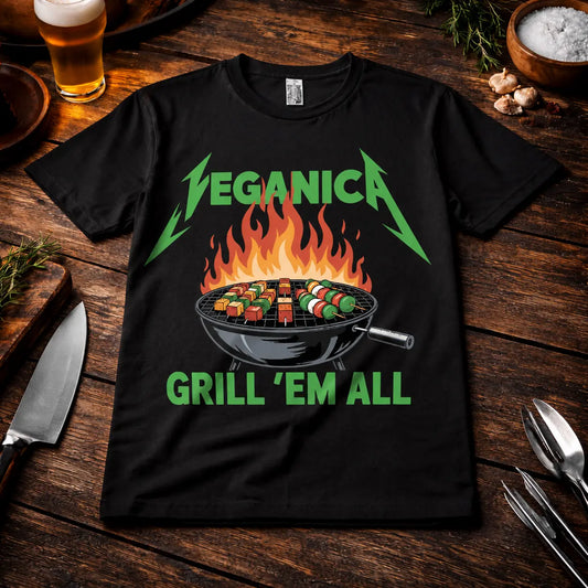 Meatware Veganica Grill 'Em All T-Shirt mit lustigem Vegan BBQ Design, brennendem Kugelgrill und Gemüse-Spießen auf schwarzem Shirt im rustikalen Grill-Mockup mit Bier, Kräutern und Grillbesteck.