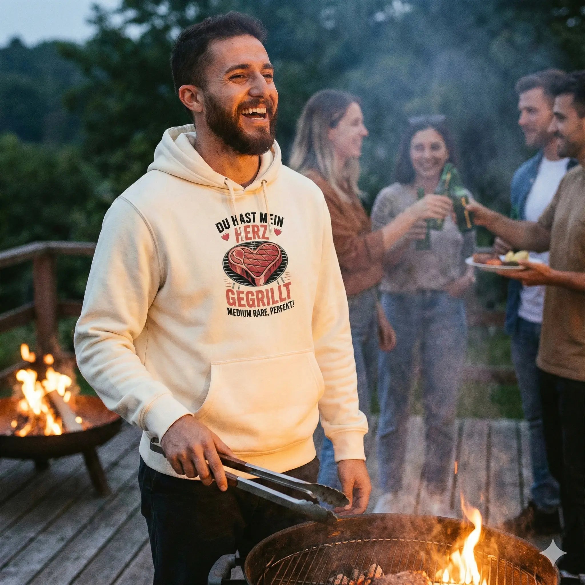 Lachender Mann am Grill in beigem Hoodie mit Herz-Steak-Motiv "Du hast mein Herz gegrillt", Abendstimmung