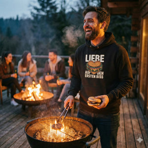 Lachender Mann am Grill in schwarzem Hoodie mit Burger-Herz-Motiv "Liebe auf den ersten Biss", gemütliche BBQ-Nacht