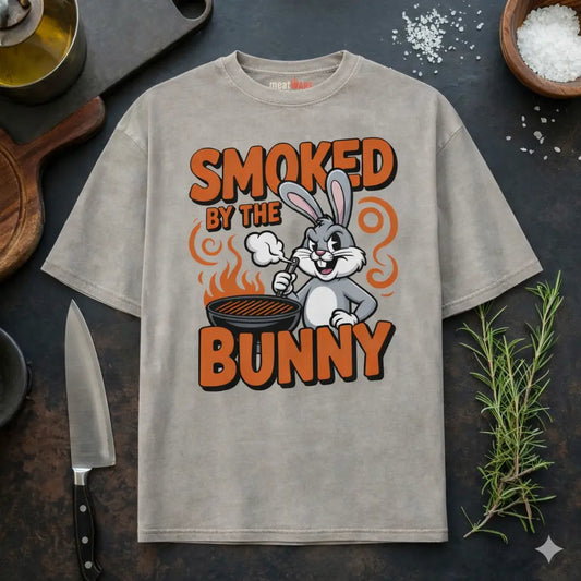 Beiges Meatware Oversized T-Shirt mit Smoked by the Bunny BBQ Hasen Grill Design und Meatware Nackenbranding auf dunklem Küchen Hintergrund mit Messer, Rosmarin und grobem Salz