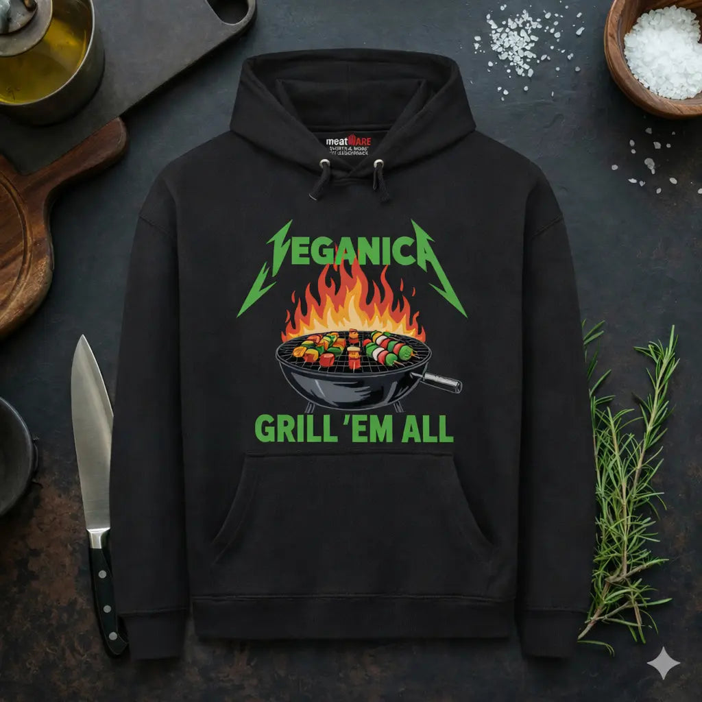 Schwarzer Meatware Premium Hoodie mit Veganica Grill ’Em All BBQ Gemüse Grill Design und Meatware Nackenbranding auf dunklem Küchen Hintergrund mit Messer, Rosmarin und grobem Salz